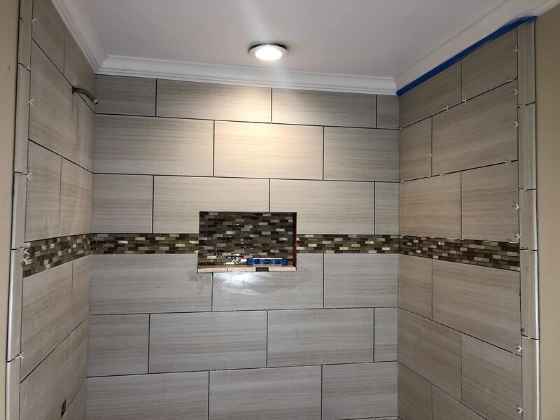 Shower tile work with mosaic accent band, corner niche, and recessed lighting